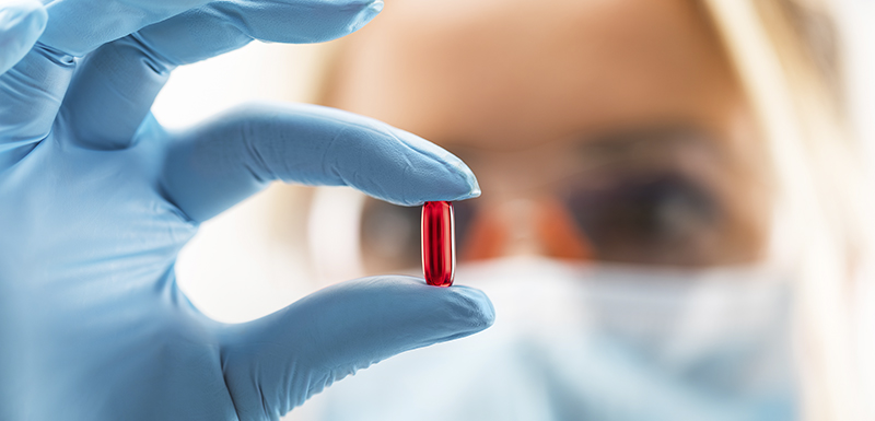 Jeune femme scientifique tenant une gélule rouge transparente contenant insuline